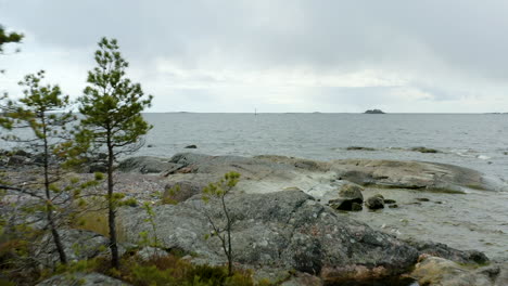 Aerial,-low,-drone-shot-between-trees,-over-the-rocks-and-cliffs-on-a-island,-in-the-archipelago-of-Porvoo,-cloudy-day,-in-Uusimaa,-Gulf-of-Finland