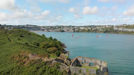 el video aéreo se desplaza a lo largo de la costa sobre un puesto avanzado abandonado para revelar un pequeño barco de pesca que se acerca y el hermoso pueblo turístico de kinsale en segundo plano.