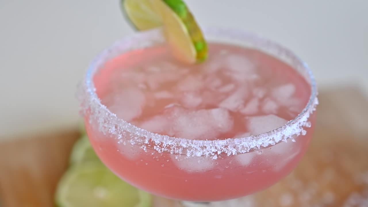 Primer plano de un cóctel rosa claro con hielo y rodajas de lima