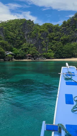 Video-Vertical,-Llegando-Con-Bote-A-Una-Playa-Vacía-Bajo-Un-Acantilado-De-Piedra-Caliza-Con-Una-Casa-Abandonada,-El-Nido,-Filipinas