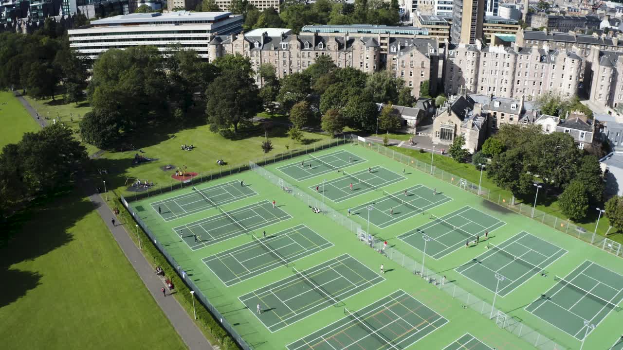 Una ripresa aerea in movimento di persone che giocano a tennis su 16 campi da tennis all'aperto, in una giornata di sole | The Meadows, Edimburgo, Scozia | 4k a 30 fps.