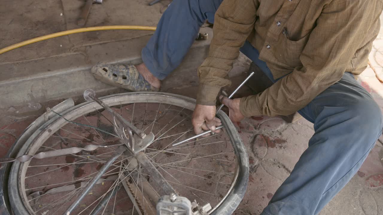 Close-up de um mecânico indiano local usando ferramentas de metal para consertar um pneu furado e raios em uma roda de bicicleta. Cena de rua autêntica mostrando trabalho manual e serviço de reparo