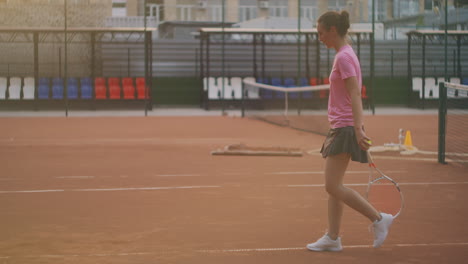 a woman walks on a tennis court with a racket and knocks the ball on the ground. concentration will to win