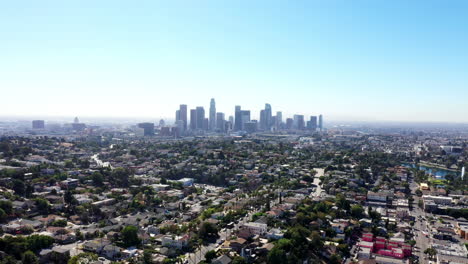 Beautiful-drone-shot-flying-high-above-neighborhoods-of-Los-Angeles,-California-showing-the-city-skyline,-palm-tree-lined-streets,-homes-and-cars