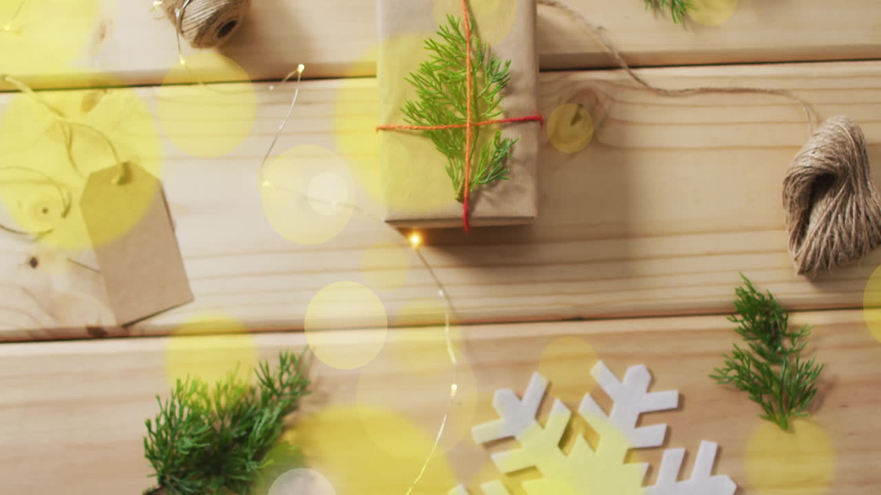 Gift wrapping and christmas decorations over yellow bokeh lights animation on wooden background