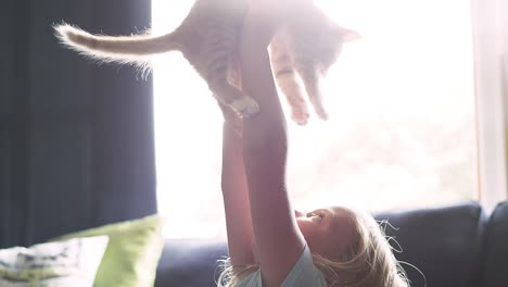 una niña pequeña sosteniendo un gato por encima de su cabeza y luego dándole un abrazo