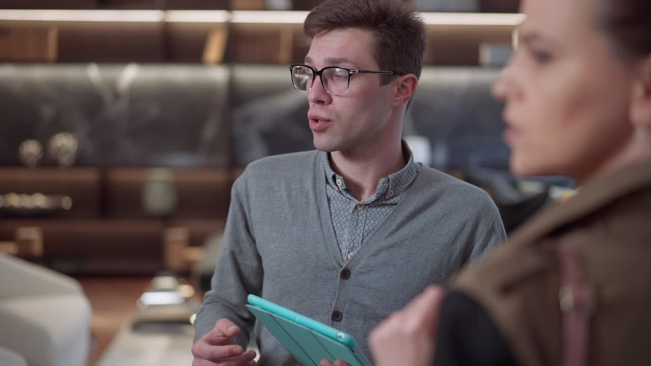 retrato de un joven vendedor confiado con gafas y tableta de pie en una tienda de muebles hablando con un cliente. experto vendedor caucásico consultando al cliente en una lujosa sala de exposiciones de la tienda en el interior.