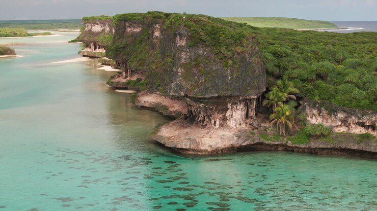 Drone shot of Lekini Bay, Ouvéa, showing clear turquoise lagoon, reef patches, limestone cliffs and lush coastal vegetation in New Caledonia