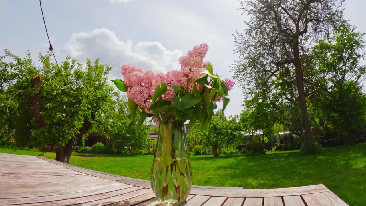 Spring bouquet in a glass vase on an outdoor table with bright garden trees and drifting clouds, captured as a calm daylight timelapse useful for weather, gardening, and lifestyle projects