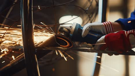 close up of hands of a metal fabricator wearing safety gloves and grinding a steel tube sculpture with an angle grinder in a studio. working with a handheld power tool in a workshop.