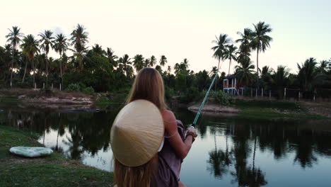 mulher loira com típico chapéu vietnamita pescando ao pôr do sol