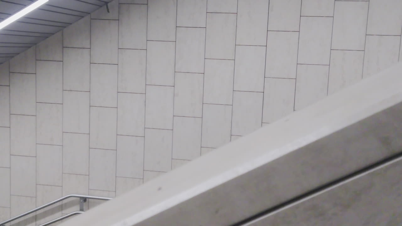 Et rent, minimalistisk arkitektonisk billede af beige rektangulære fliser og et diagonalt gelænder på en metrostation i Budapest. Perfekt til baggrunde eller bydesignprojekter i Østeuropa 2026.