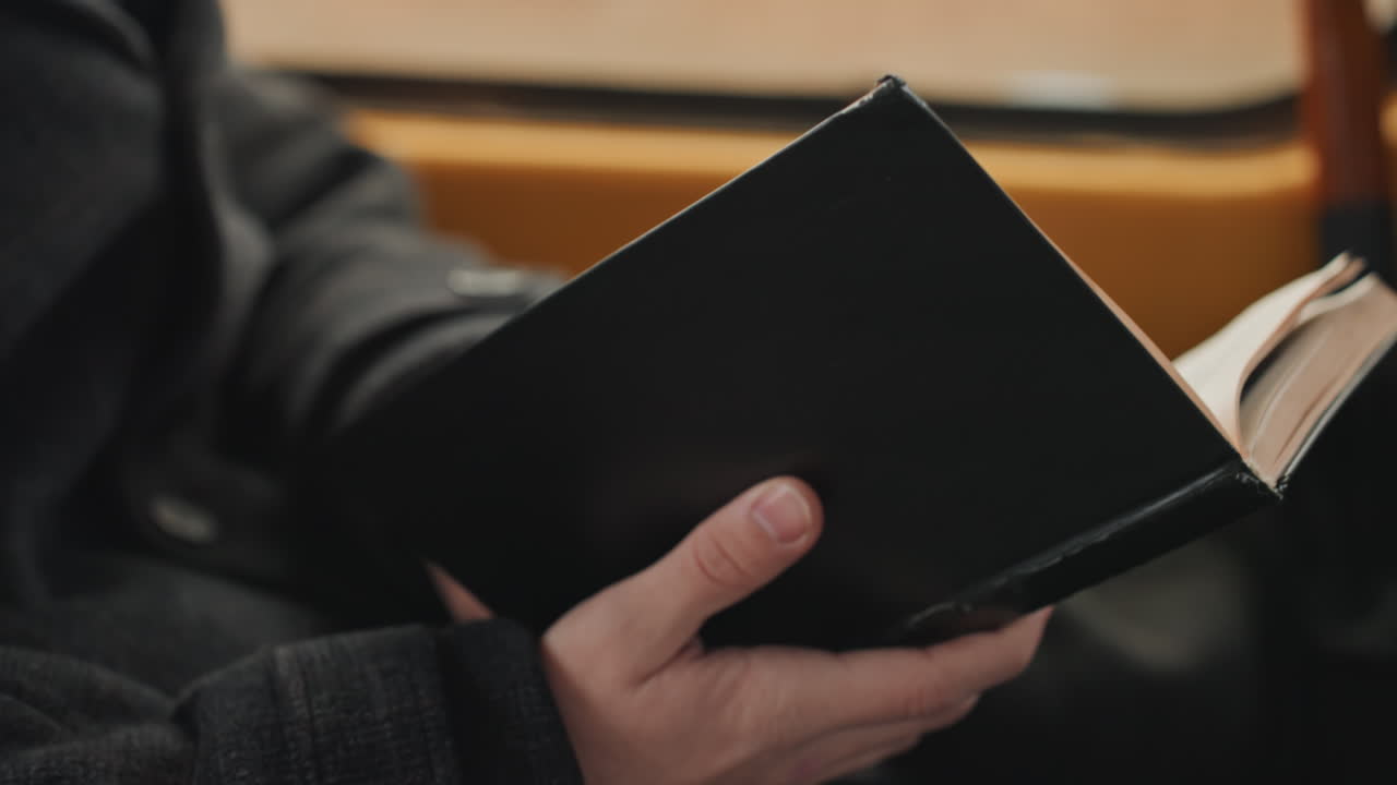 Mani che tengono un quaderno sul treno, creatore che legge in silenzio con un maglione comodo, pagine rilegate in pelle che si girano alla luce del finestrino, mani concentrate e atmosfera di pendolarismo lento, umore riflessivo e sottile ispirazione.