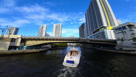motor boat sails under the bridge in modern city. low angle view at the high-rise houses from fpv drone.