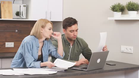 caucasian young couple reading and analyzing bills sitting at table