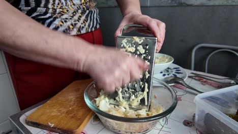 an elderly woman grates an apple for a fruit and vegetable salad on an old traditional grater