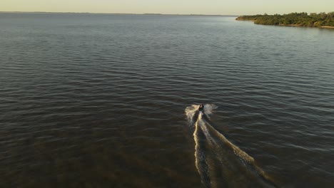 slow motion aerial view behind jetski on lake during sunset