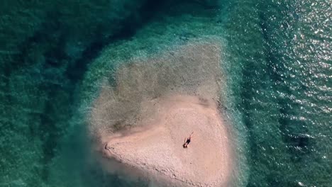 top-down shot of a beautiful caucasian woman sunbathing on a small island in italy surrounded by bright blue sea on a summer day - aerial