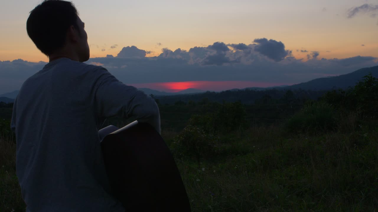 베트남 일몰 직전에 기타를 연주하는 남성 음악가의 어깨 너머로 보이는 풍경