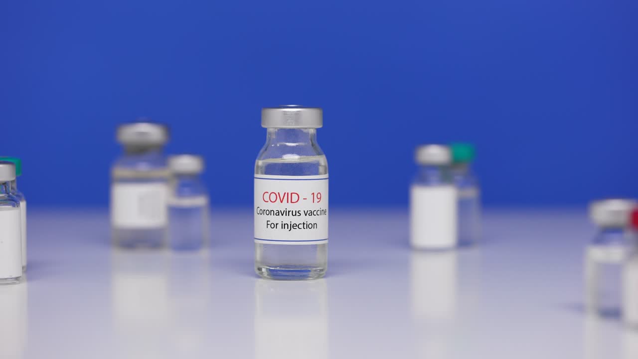 botella de vacuna contra el virus sars-cov-2 en la mesa de laboratorio de fondo. ampollas de primer plano con la vacuna del coronavirus covid-19. medicamentos contra la pandemia de ncov. pantalla azul, llave de croma. primer plano. cámara lenta