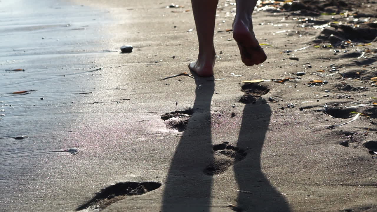 Person Walking Barefoot on a Sandy Beach at Sunset Leaving Footprints