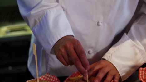 Happy-chef-placing-skewers-on-burger-in-kitchen