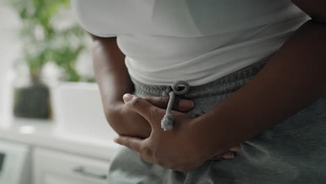 young african-american woman standing in the bathroom and feeling pain in the stomach.