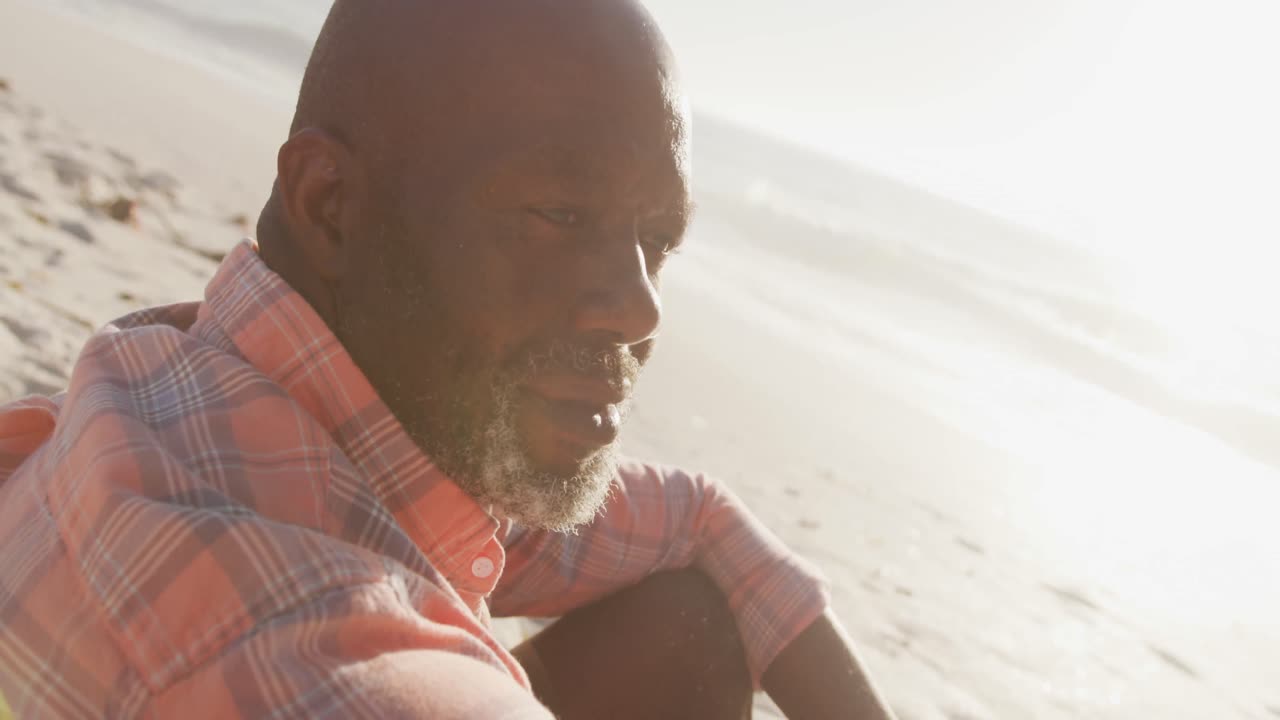 Senior african american man wearing shirt and sitting on sunny beach