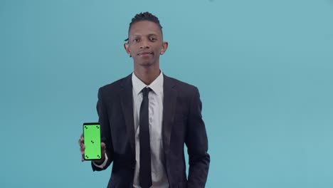 black male businessman in a strict office suit holds a phone with an app and smiles positively nods head in the studio, blue background. concept of apps and corporate advertising