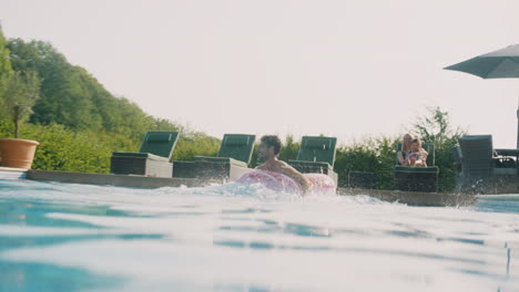 underwater shot of father with inflatable ring jumping into swimming pool on family summer vacation