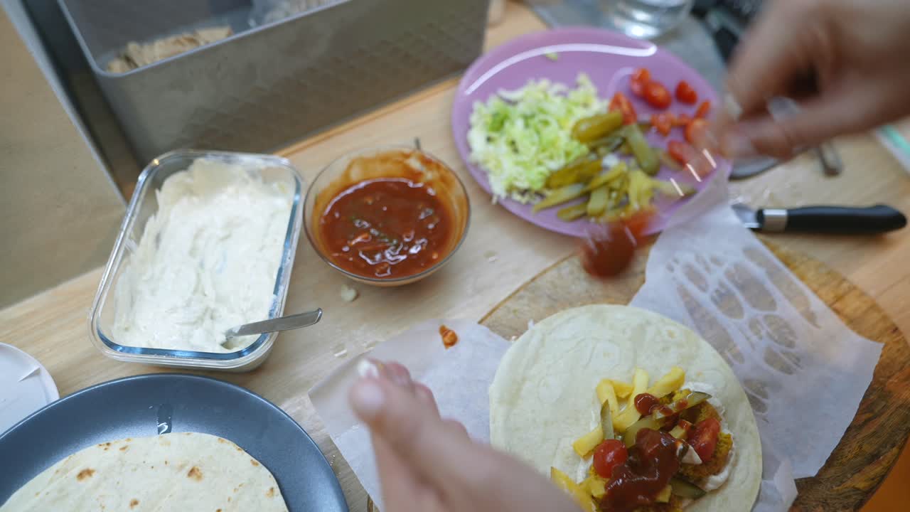 Person's Hands Assembling a Falafel Wrap with French Fries