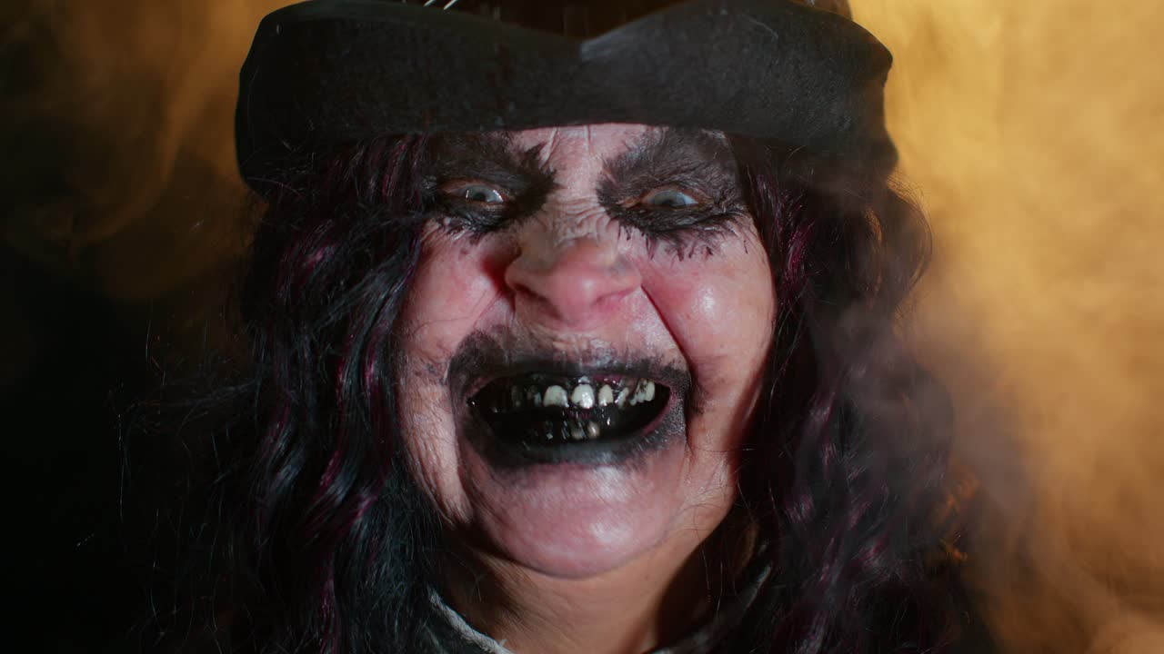 Sinister senior mature woman in carnival costume of Halloween witch making faces, trying to scare