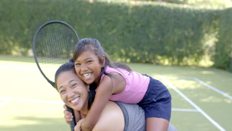 playing on tennis court, mother carrying daughter on back, both smiling happily