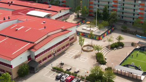 Beautiful-school-building-and-yard-in-suburbs-of-Stockholm-near-living-buildings,-aerial-drone-fly-back-view