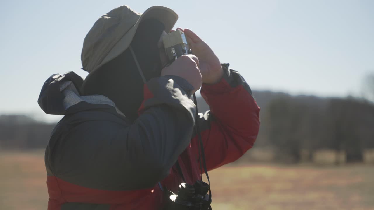 Uomo nella natura che scatta fotografie e osserva con il binocolo.
