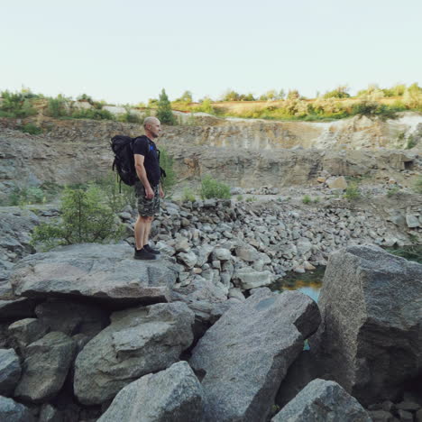 a tourist in summer clothes walks on the edge of a quarry with huge stones and looks at the beautiful lake and the nature around it. beautiful view.