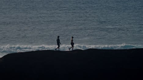 A young couple walks hand in hand along a rugged volcanic cliff overlooking the Atlantic Ocean in Lanzarote, Canary Islands, Spain.