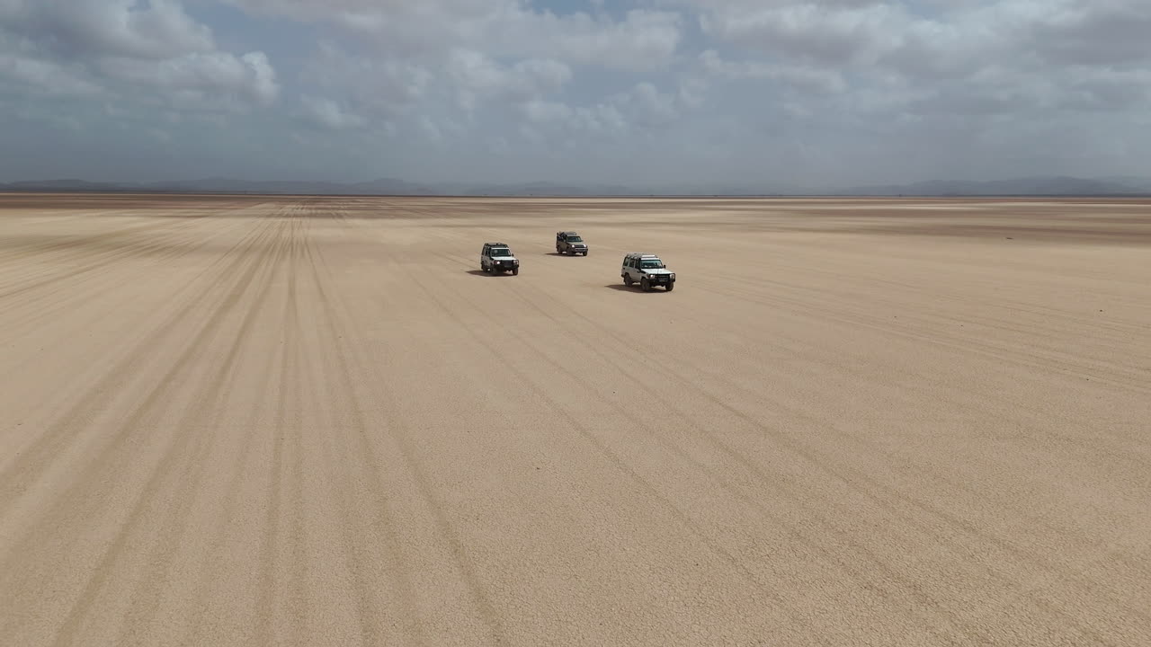 Riprese aeree di veicoli che viaggiano attraverso un ambiente desertico ostile con polvere, ripresa da drone rotante. Gibuti, Africa.
