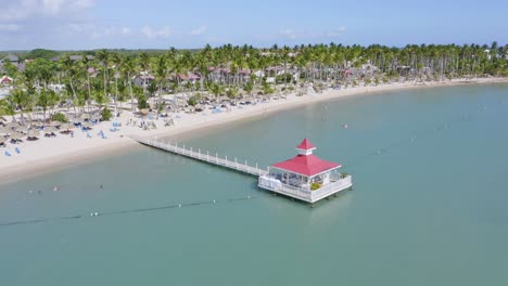 Aerial-forward-flight-over-jetty-along-sandy-beach-with-sunshades-and-tropical-palm-trees---BAHIA-PRINCIPE-GRAND-LA-ROMANA,Dominican-Republic