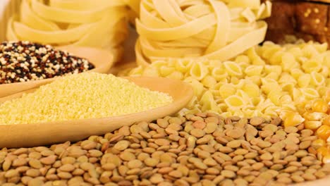 various grains and pasta displayed with warm lighting, highlighting textures and colors. includes quinoa, lentils, tagliatelle, and corn