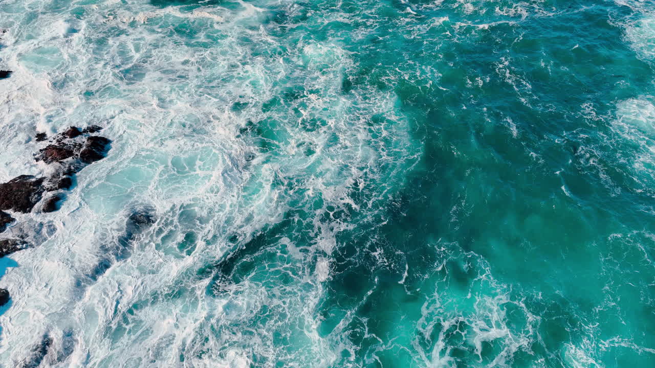 Vista dall'alto dell'acqua del mare turchese con la schiuma bianca delle onde. Prospettiva dall'alto dell'acqua dell'oceano vibrante, blu e verde, che forma vortici con la risacca bianca.
