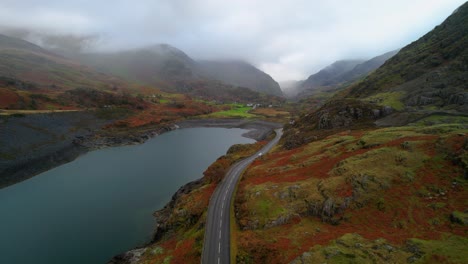 Conducción-De-Automóviles-En-La-Carretera-A-Lo-Largo-Del-Lago-De-La-Cantera-Dinorwic-Con-Montañas-Envueltas-En-Nubes-En-El-Fondo,-Gales-En-El-Reino-Unido