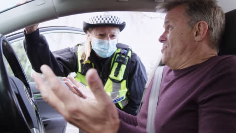 angry male driver being stopped by female traffic police officer wearing mask for driving offence