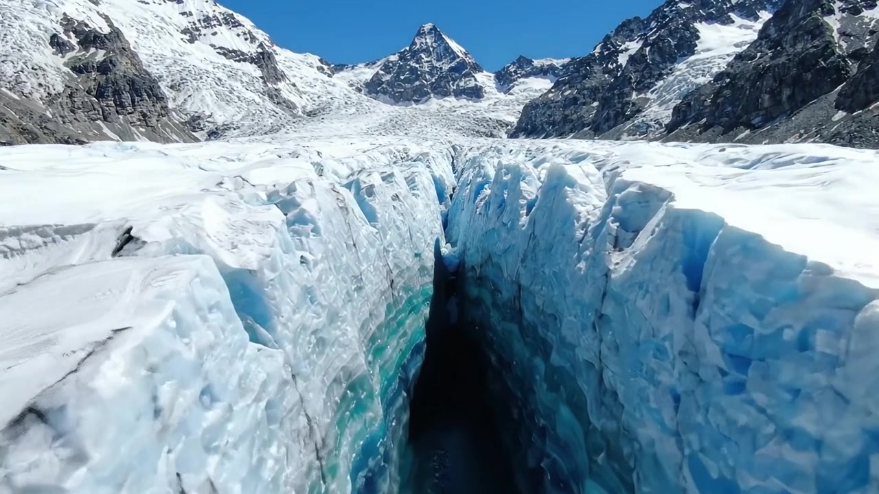 Stunning Aerial View of a Majestic Glacier Split, Revealing Deep Blue Ice Crevasses and Towering Snow-Capped Mountains Under Bright Sunlight