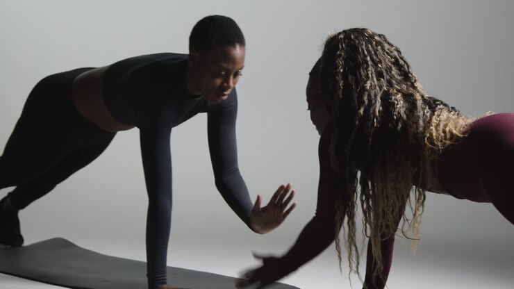Studio Shot Of Two Women Wearing Gym Fitness Clothing Facing Each Other Exercising