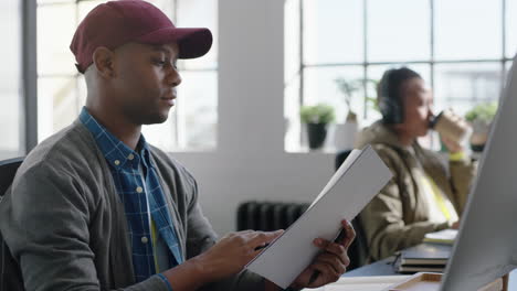 Feliz-Hombre-De-Negocios-Afroamericano-Leyendo-Documentos-Corporativos-Intercambiando-Ideas-Escribiendo-Notas-Usando-Una-Estrategia-De-Planificación-Informática-Disfrutando-De-Una-Carrera-Exitosa-En-Una-Moderna-Empresa-De-Comunicación-De-Inicio