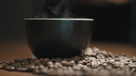 steam over a cup of coffee on a wooden table surrounded by fresh coffee beans slow motion