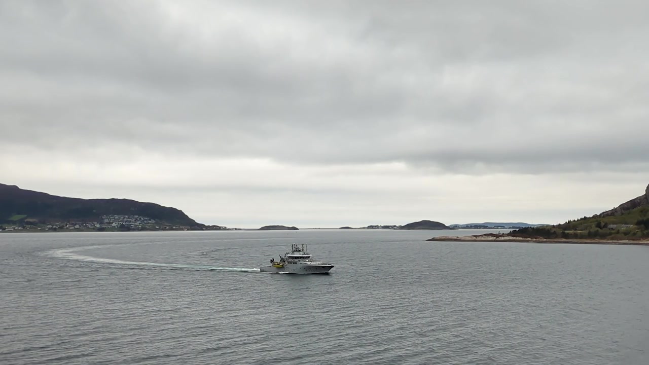 Motoryacht grigio che naviga su acque calme ad Ålesund, con le montagne sullo sfondo, Norvegia