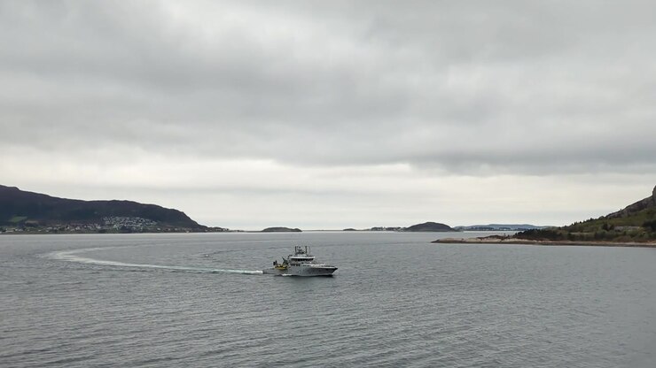 Motoryacht grigio che naviga su acque calme ad Ålesund, con le montagne sullo sfondo, Norvegia