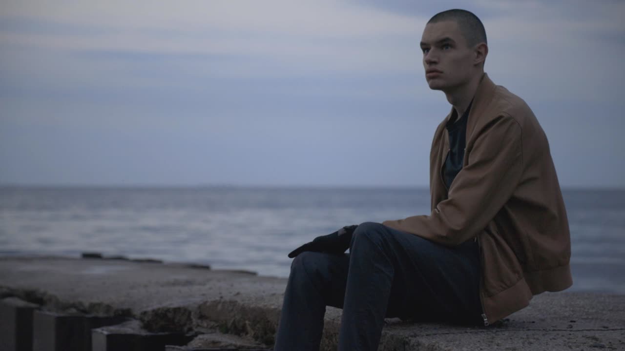 A Lonely Young Man Sitting On The Pier While Looking On Around - Close Up Shot